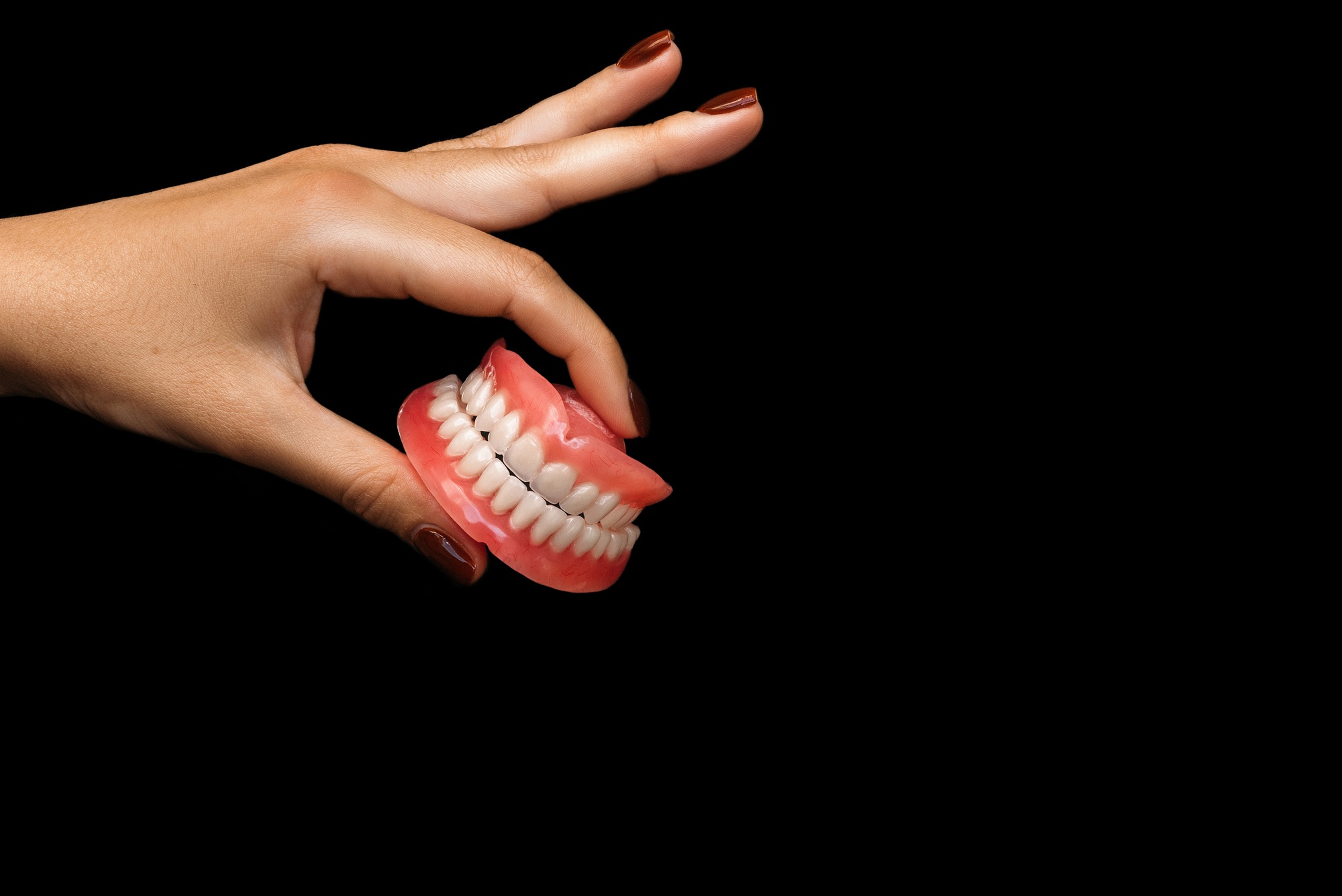 Denture in hand. False teeth in the hand. Denture on a black background