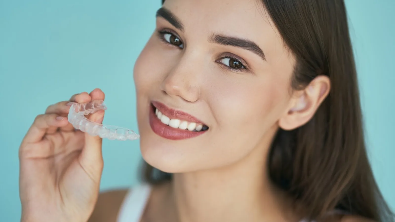 Una mujer sonríe mientras sostiene un alineador dental transparente frente a la cámara
