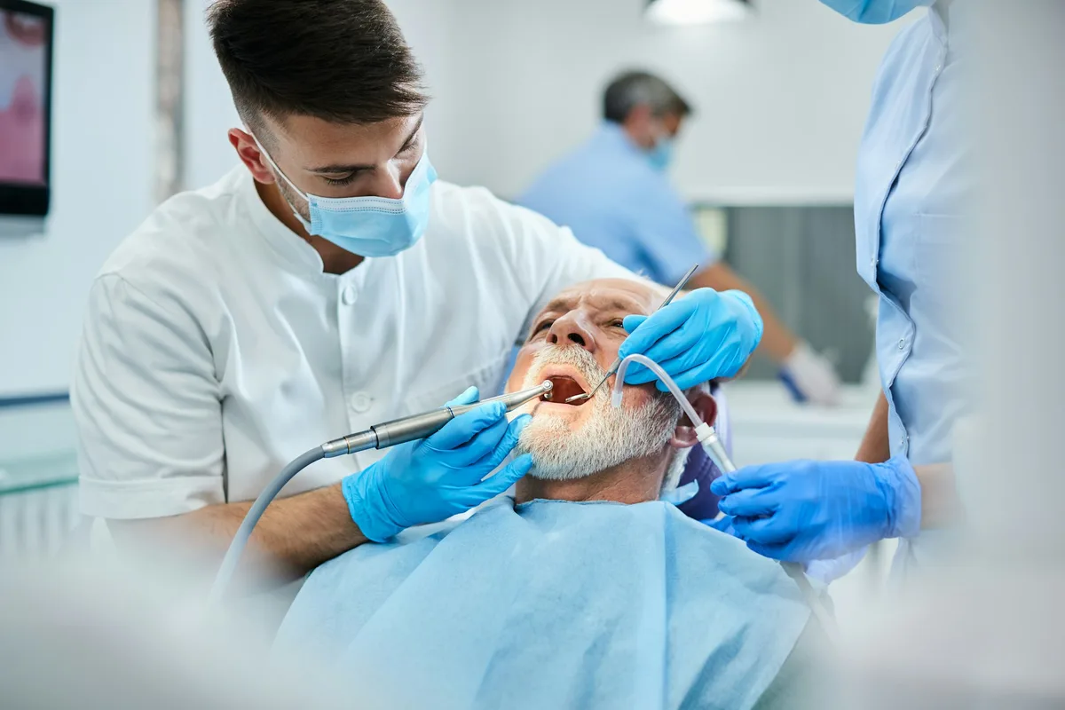 Limpieza Dental en Tamarac: Qué Incluye la Primera Visita y Cada Cuánto Volver 2 Un odontólogo realiza una limpieza dental a un paciente mayor recostado en el sillón