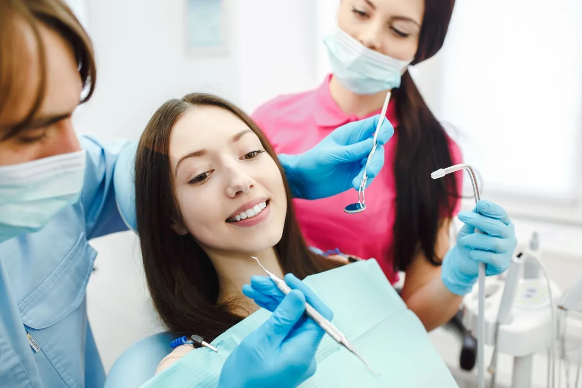 A dental hygienist works on a patient reclined in the chair while an assistant holds the light