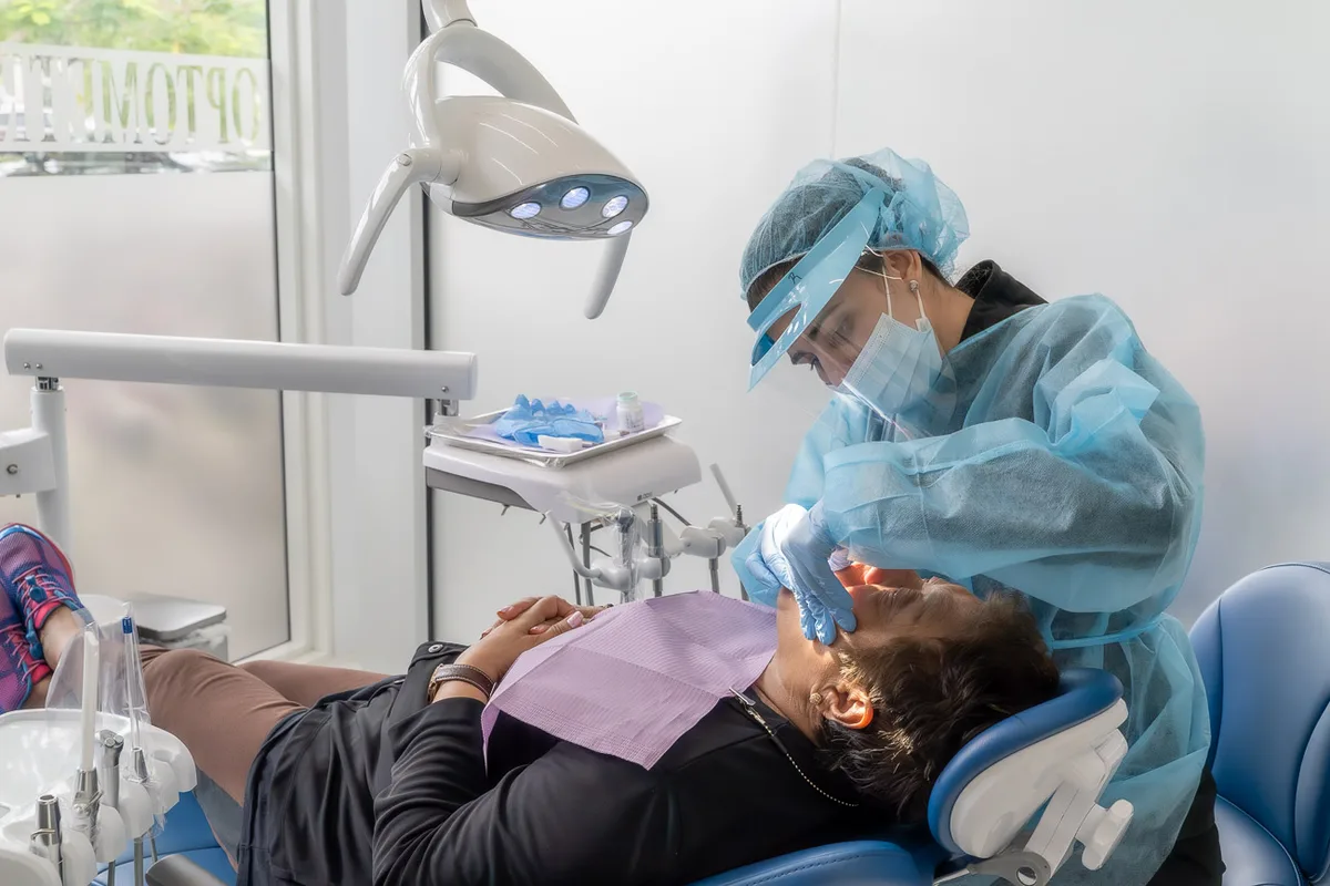 Diente Roto en Tamarac: Qué Hacer en las Primeras Horas y Cómo se Arregla 3 Personal dental con careta y bata protectora atiende a un paciente en el sillón del consultorio, con ventanales al fondo