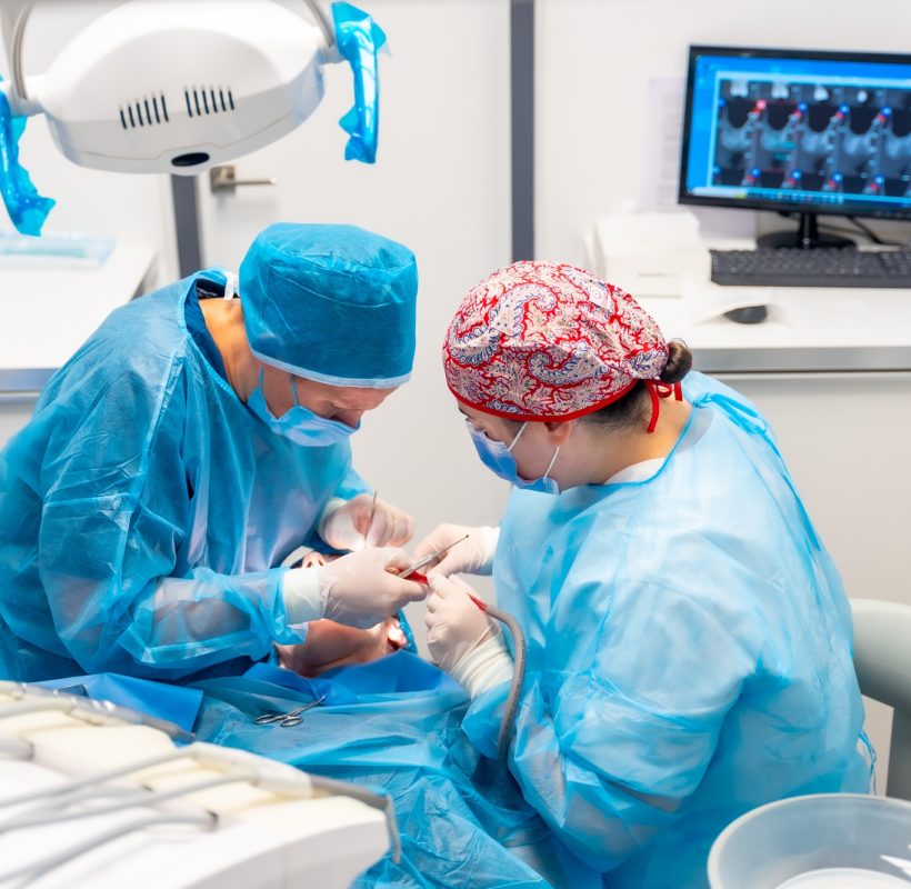 Female dentists in blue scrubs performing a complicated operation on a female patient, sucking blood Female dentists in blue scrubs performing a complicated operation on a female patient, sucking blood