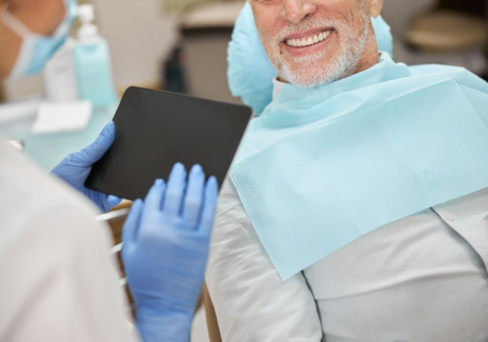 Senior gentleman smiling at the dentist holding a tablet